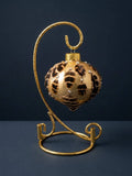 Gold glass onion Christmas ornament covered in pheasant feathers with Swarovski crystals, shown on a gold display stand